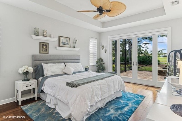 bedroom with hardwood / wood-style floors, a tray ceiling, access to outside, and ceiling fan