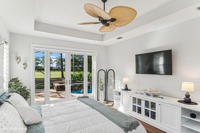 bedroom featuring hardwood / wood-style floors, access to outside, ceiling fan, a tray ceiling, and french doors