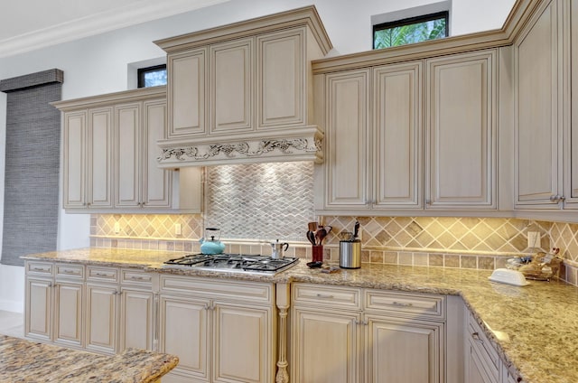 kitchen featuring crown molding, backsplash, light stone countertops, cream cabinetry, and stainless steel gas stovetop