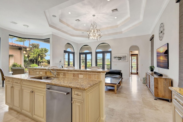 kitchen featuring sink, light stone counters, decorative light fixtures, a kitchen island with sink, and cream cabinetry