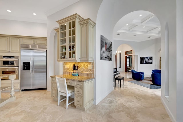 kitchen with stainless steel appliances, coffered ceiling, light stone countertops, and cream cabinets