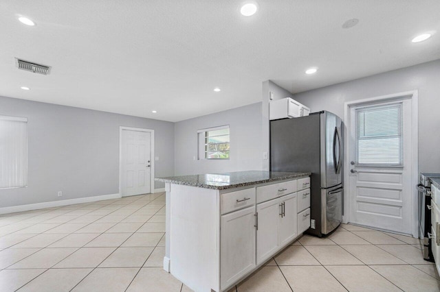 kitchen featuring stainless steel refrigerator, dark stone countertops, white cabinets, light tile patterned floors, and a textured ceiling