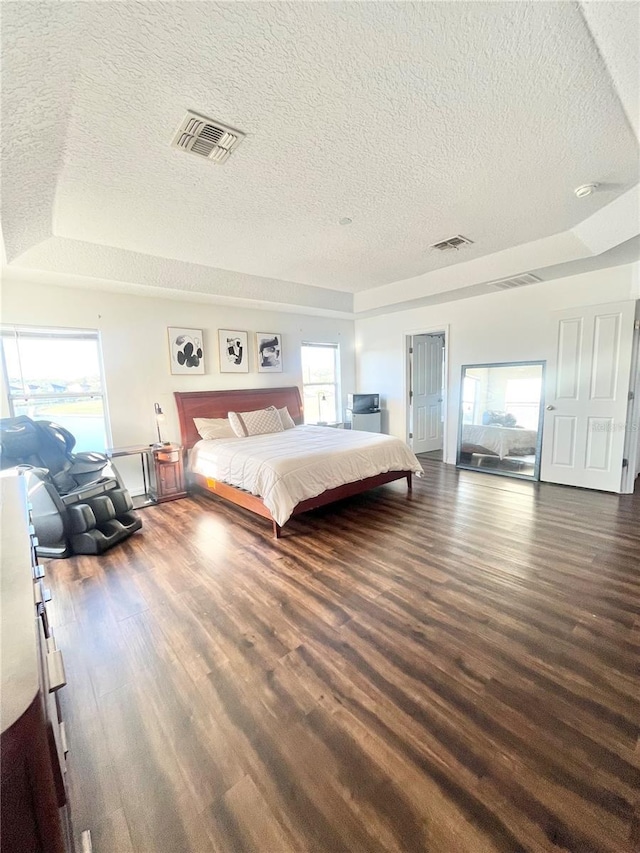 bedroom featuring a textured ceiling, dark wood-type flooring, multiple windows, and a tray ceiling