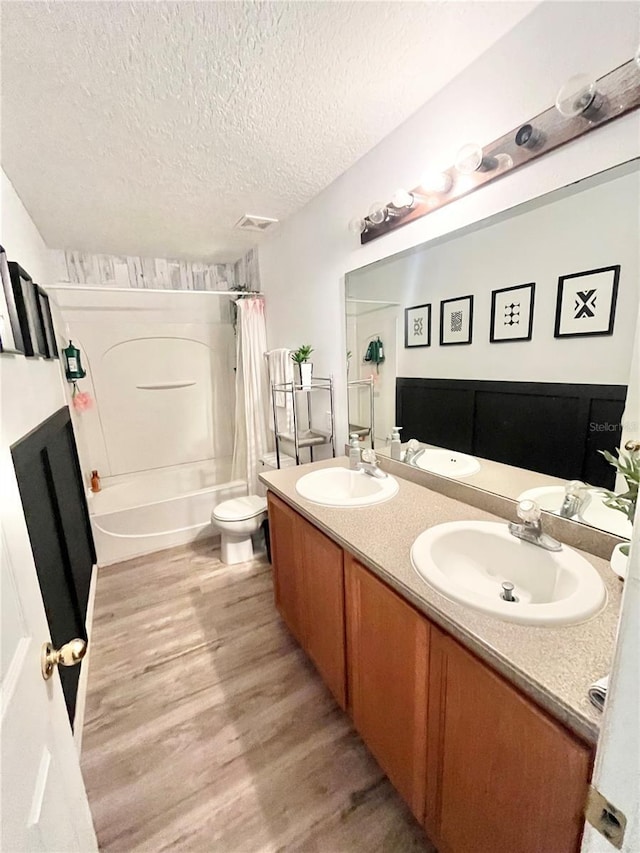 full bathroom with shower / tub combo, hardwood / wood-style floors, a textured ceiling, toilet, and vanity