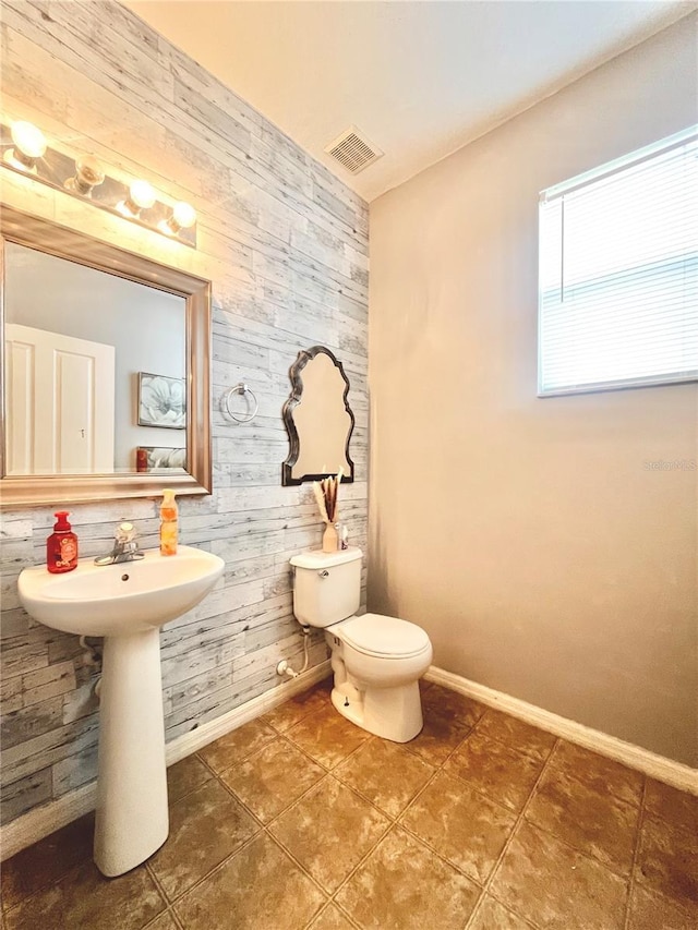 bathroom with tile patterned floors, toilet, and wood walls