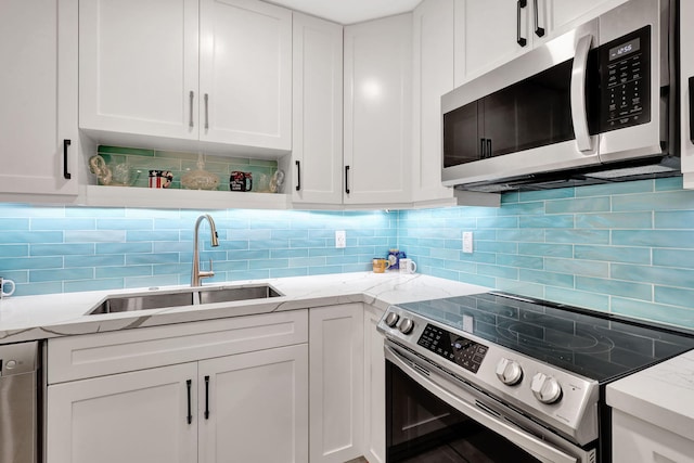 kitchen with light stone countertops, white cabinetry, sink, and stainless steel appliances