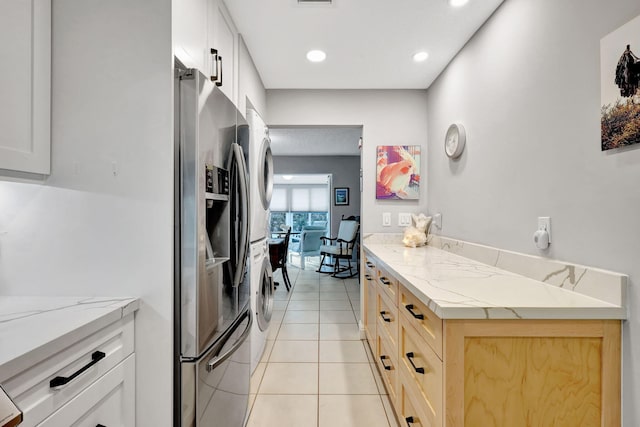 kitchen featuring white cabinets, stainless steel fridge with ice dispenser, stacked washing maching and dryer, light stone counters, and light tile patterned floors