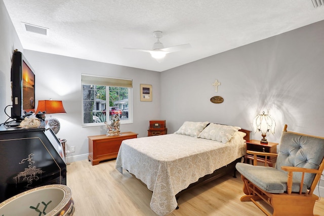 bedroom with light wood-type flooring, ceiling fan, and a textured ceiling