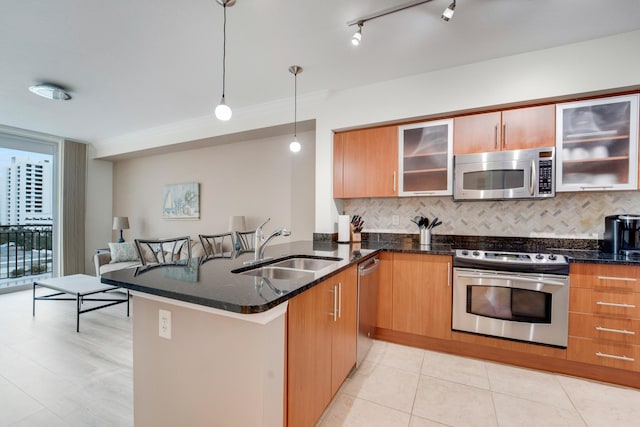 kitchen featuring appliances with stainless steel finishes, dark stone countertops, sink, hanging light fixtures, and kitchen peninsula