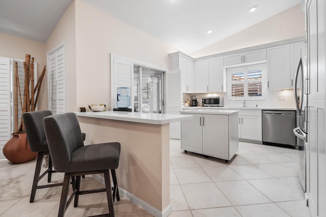 kitchen with white cabinetry, a breakfast bar area, stainless steel appliances, vaulted ceiling, and a center island