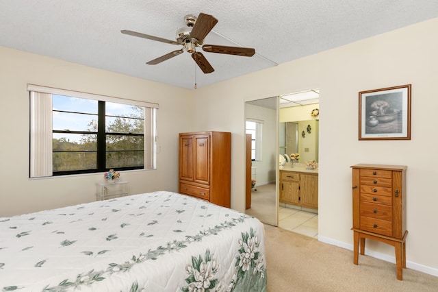 bedroom with ceiling fan, ensuite bathroom, a textured ceiling, light carpet, and a closet