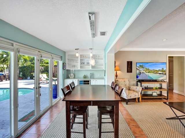 dining area with tile patterned flooring, wine cooler, and a textured ceiling