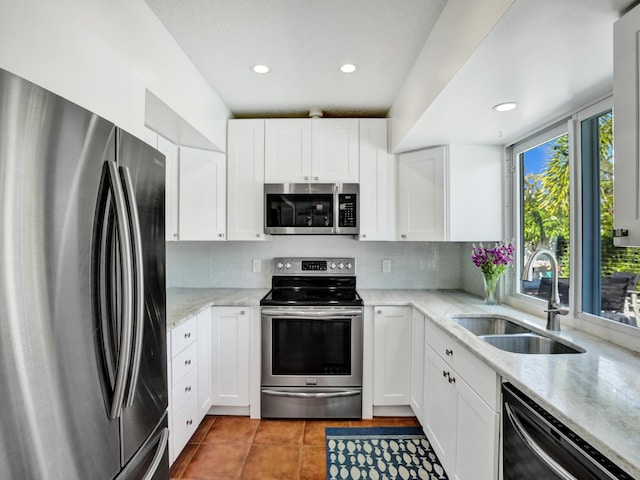 kitchen with sink, appliances with stainless steel finishes, white cabinetry, light tile patterned flooring, and decorative backsplash