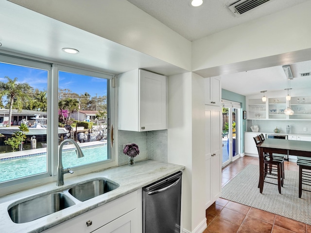 kitchen with tasteful backsplash, sink, white cabinets, stainless steel dishwasher, and light stone countertops