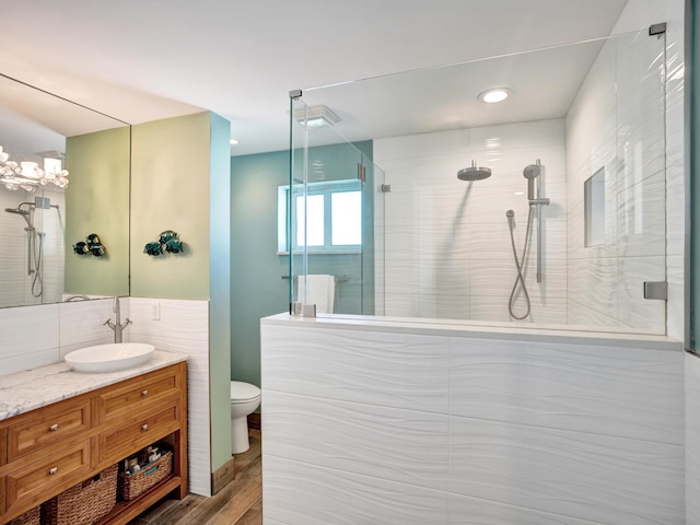 bathroom featuring tiled shower, toilet, tile walls, vanity, and hardwood / wood-style flooring