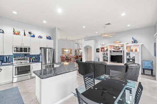 kitchen featuring light tile patterned floors, dark stone counters, stainless steel appliances, white cabinets, and tasteful backsplash