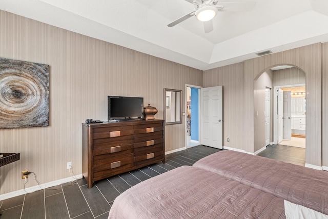 bedroom with ceiling fan, connected bathroom, a tray ceiling, and dark hardwood / wood-style flooring