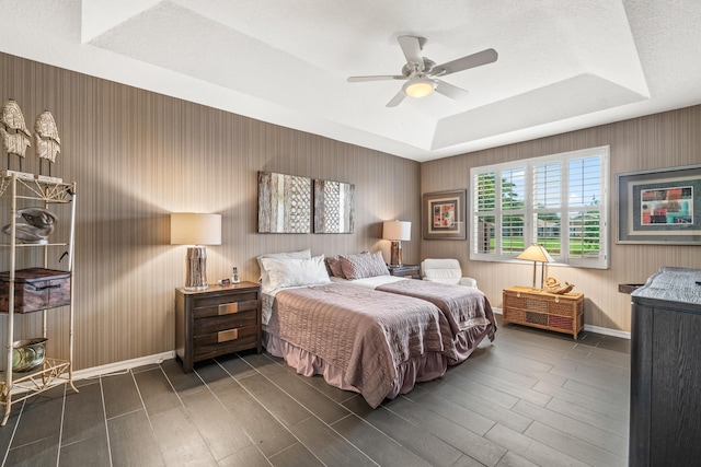 bedroom with a tray ceiling, ceiling fan, dark hardwood / wood-style floors, and a textured ceiling