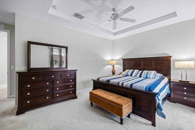 bedroom with ceiling fan, light colored carpet, and a tray ceiling