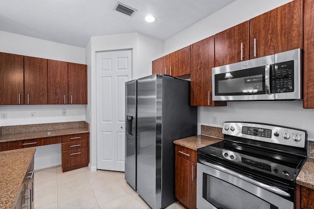 kitchen featuring light tile patterned floors, appliances with stainless steel finishes, built in desk, and dark stone counters