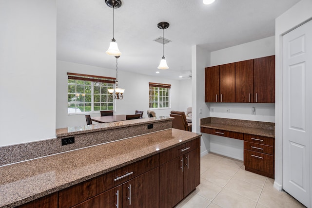 kitchen with built in desk, dark stone countertops, hanging light fixtures, light tile patterned flooring, and dark brown cabinets