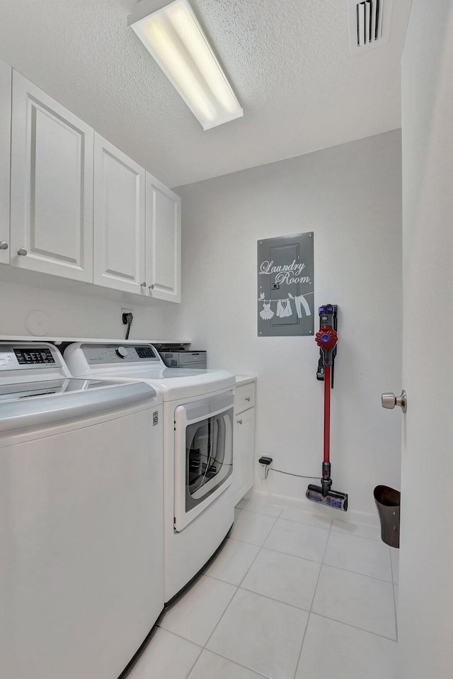 washroom with washing machine and dryer, a textured ceiling, cabinets, and light tile patterned flooring