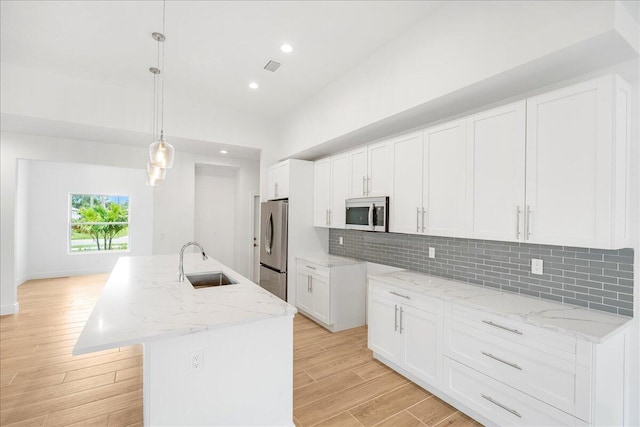 kitchen featuring decorative light fixtures, a center island with sink, sink, white cabinetry, and appliances with stainless steel finishes