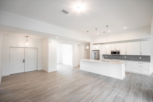 kitchen featuring a center island with sink, appliances with stainless steel finishes, decorative backsplash, decorative light fixtures, and white cabinets