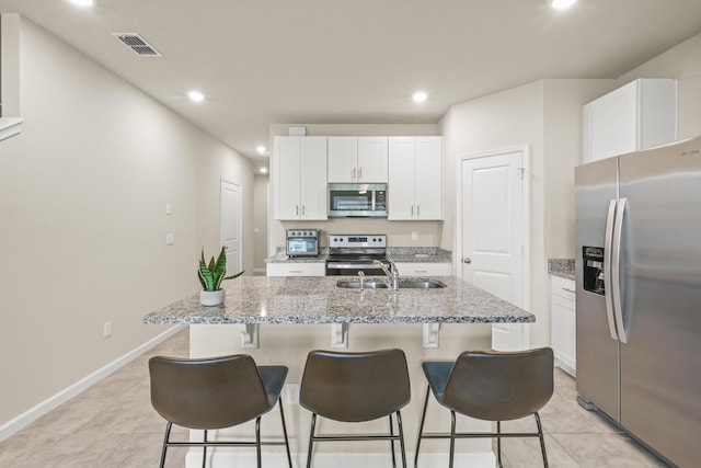 kitchen featuring white cabinetry, a kitchen island with sink, sink, stainless steel appliances, and light stone counters