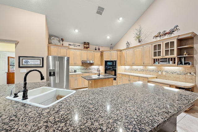 kitchen with a center island with sink, under cabinet range hood, tasteful backsplash, a sink, and black appliances