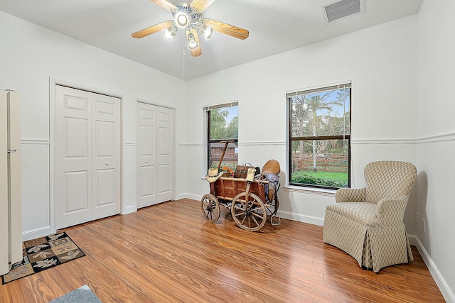living area with light wood-style floors, baseboards, ceiling fan, and visible vents