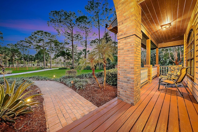 deck at dusk with a lawn and covered porch