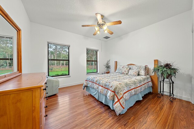 bedroom featuring baseboards, ceiling fan, multiple windows, and wood finished floors