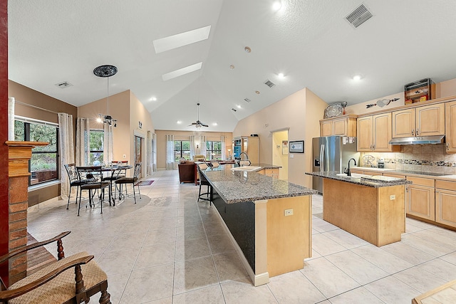 kitchen featuring dark stone countertops, sink, hanging light fixtures, light tile patterned flooring, and a center island with sink