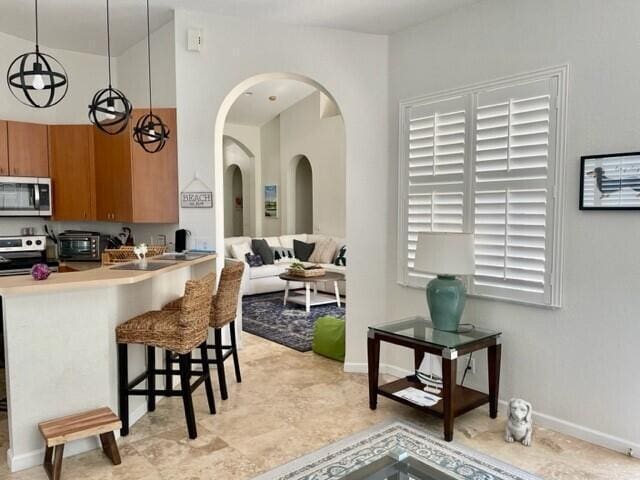 kitchen with hanging light fixtures, appliances with stainless steel finishes, kitchen peninsula, and a breakfast bar area