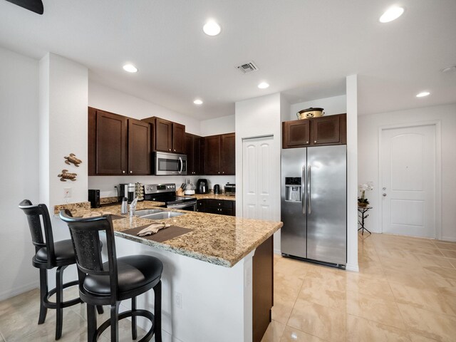 kitchen featuring a kitchen bar, stainless steel appliances, sink, kitchen peninsula, and dark brown cabinets