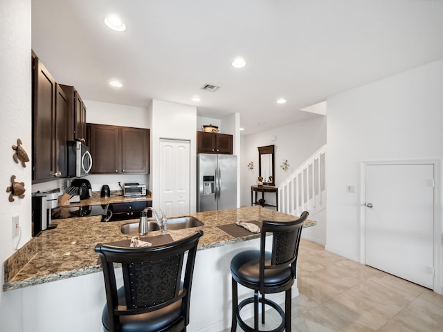 kitchen with stainless steel appliances, sink, a kitchen breakfast bar, light stone counters, and dark brown cabinets