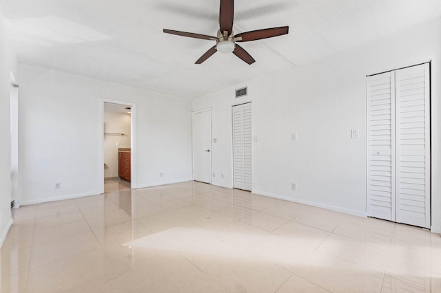 unfurnished bedroom with ceiling fan, connected bathroom, and two closets