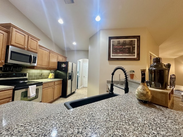 kitchen featuring appliances with stainless steel finishes, backsplash, light stone counters, and sink