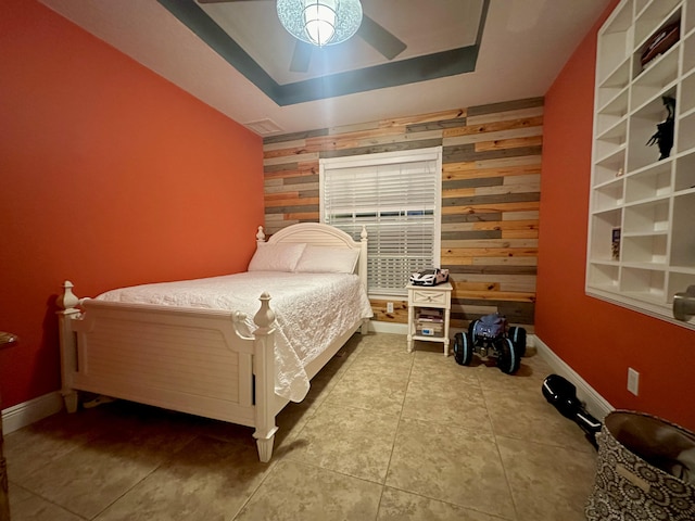 tiled bedroom featuring ceiling fan, wooden walls, and a raised ceiling