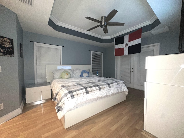 bedroom featuring ceiling fan, wood-type flooring, a tray ceiling, and ornamental molding