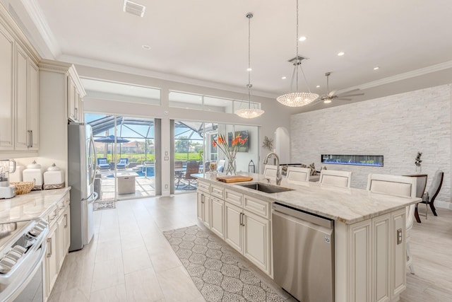 kitchen featuring sink, appliances with stainless steel finishes, pendant lighting, light stone countertops, and a kitchen island with sink