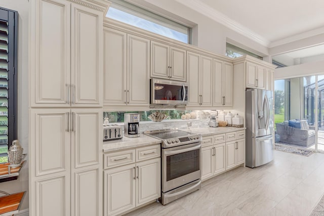 kitchen with light stone counters, ornamental molding, cream cabinetry, and appliances with stainless steel finishes