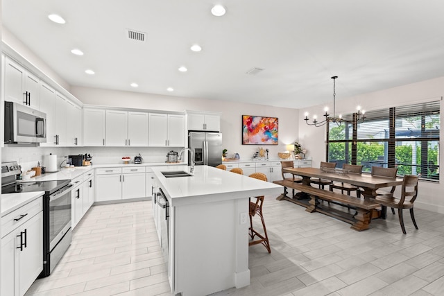 kitchen featuring a center island with sink, stainless steel appliances, pendant lighting, white cabinets, and sink