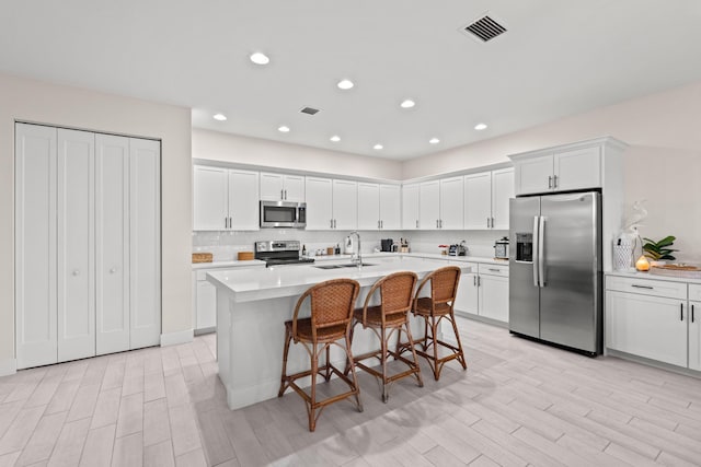 kitchen featuring appliances with stainless steel finishes, a kitchen island with sink, white cabinets, a breakfast bar, and sink