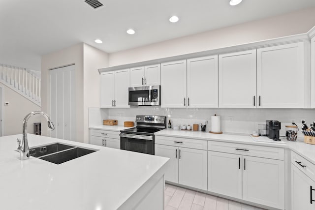 kitchen featuring white cabinetry, stainless steel appliances, backsplash, light hardwood / wood-style flooring, and sink