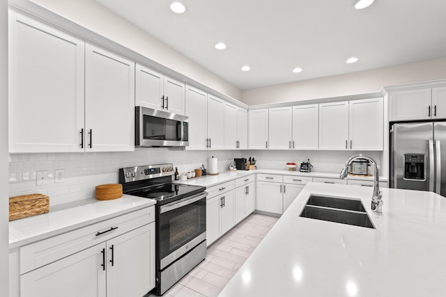 kitchen with tasteful backsplash, white cabinets, appliances with stainless steel finishes, and sink