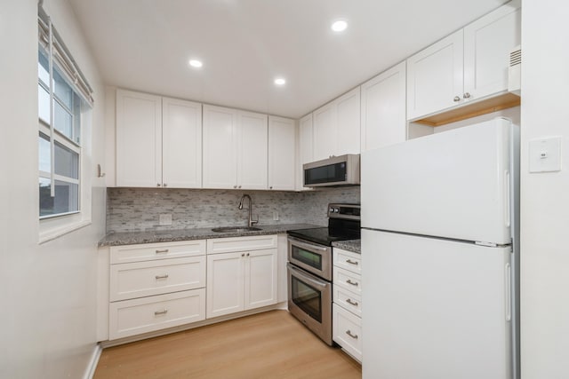 kitchen with appliances with stainless steel finishes, white cabinetry, light hardwood / wood-style floors, sink, and stone counters