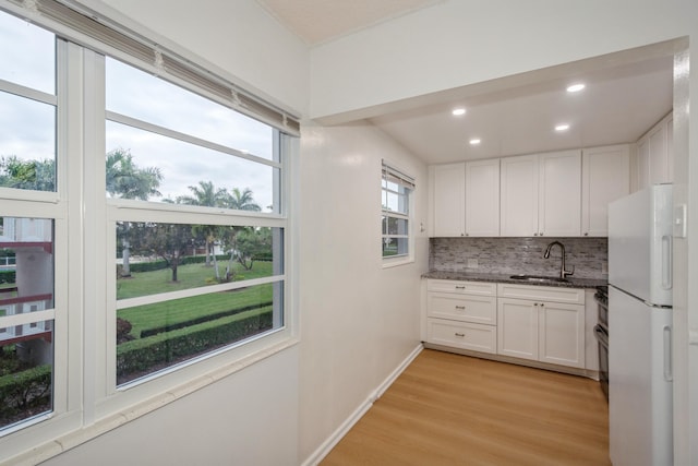 kitchen with white refrigerator, white cabinetry, sink, and backsplash