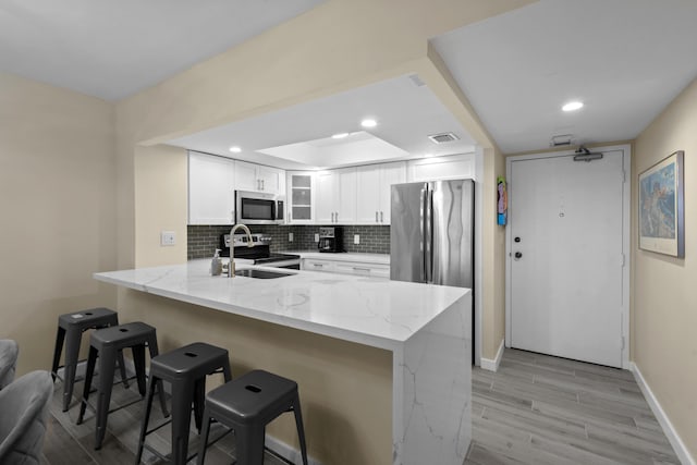 kitchen featuring light stone countertops, white cabinets, appliances with stainless steel finishes, kitchen peninsula, and a breakfast bar area